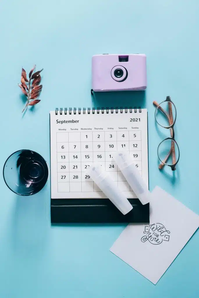 Top view of a calendar with a camera, glasses, and leaves on a pastel blue background.