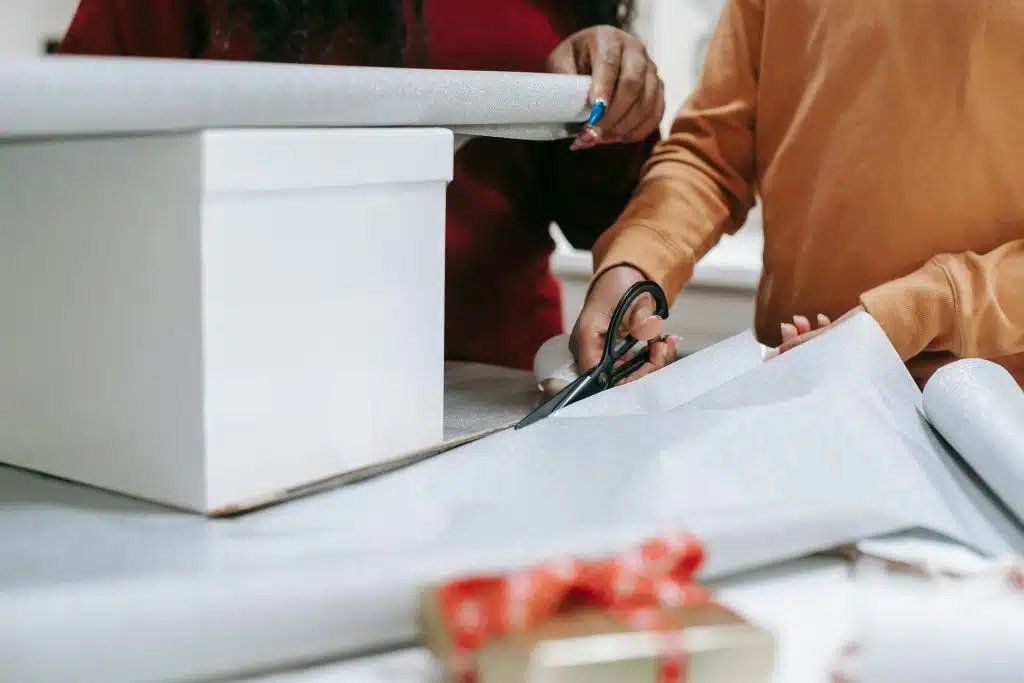 Two people wrapping a Christmas gift with scissors and wrapping paper, evoking holiday spirit.